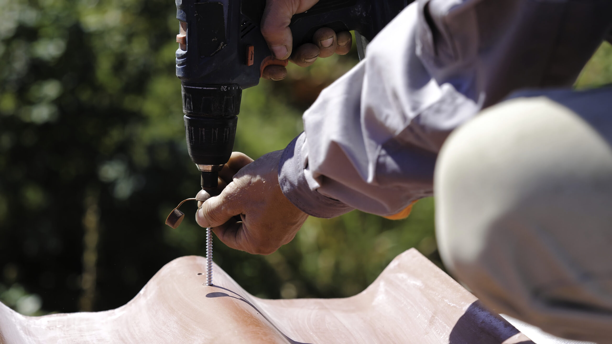 Man screws a screw into the roof. Stock footage. The professional worker works on installation of a roof of a roof by sheets of a metal tile and drills a screw with a drill